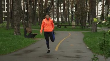 Kadın parkta koşmadan önce ısınıyor ve ısınıyor. Koşmadan önce kadın bacaklarını dışarı açıyor. Yağmurlu bir günde kadın sporcu boş parkta geriniyor. Sağlıklı yaşam tarzı kavramı