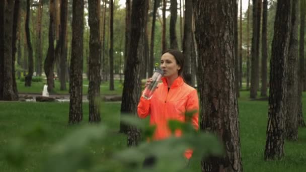 Sportiv kvinna dricker vatten ur träningsflaskan efter löpträning utomhus i parken. Porträtt av attraktiv brunett kvinna dricksvatten efter hård träning på frisk luft i parken — Stockvideo