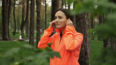 Kulaklık takan çekici esmer kadının portresi yağmurlu bir günde şehir parkında koşmaya başlıyor. Bayan sporcu kulaklık takar ve açık havada temiz hava eğitimi sırasında müzik dinler.