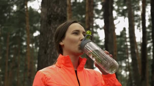 Молодая женщина пьет воду в парке. Спортивная женщина пьет воду из бутылки после тренировки на открытом воздухе. Женщина-атлет питьевая вода после бега — стоковое видео