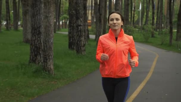 Una corredora corriendo en el parque de la ciudad. Entrenamiento femenino de fitness solo en el parque el día lluvioso. Atleta deportivo haciendo ejercicio por la mañana en la zona de recreo en el bosque. Estilo de vida saludable y concepto de funcionamiento — Vídeos de Stock