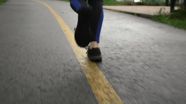 Runner woman feet in sneakers jogging in the city park. Sportswoman in sports shoes running on footpath in the park on rainy day. Healthy lifestyle and sport concept — Stock Video
