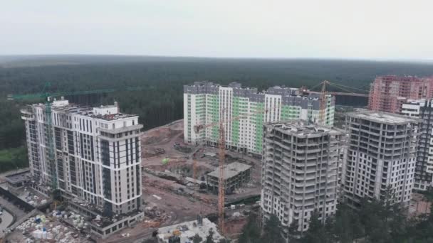 สถานที่ก่อสร้างพร้อมเครน เครนสูงพร้อมอาคารใหม่ ตึกระฟ้าภายใต้การก่อสร้างด้วยเครนขนาดใหญ่ พื้นที่อาคารสูงที่อยู่อาศัยที่ซับซ้อนทันสมัยในพื้นที่สีเขียวล้อมรอบด้วยป่า — วีดีโอสต็อก