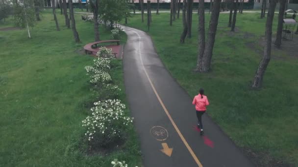 Fitness-Frau joggt an regnerischem Tag allein im Stadtpark. Sportlerin läuft auf Fußweg im Stadtpark. Frauentraining im Freien. Drohnenschuss aus der Luft — Stockvideo