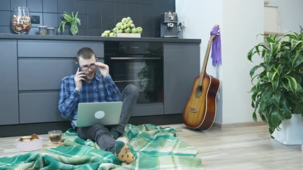 Jeune freelance homme travaillant sur ordinateur portable de la maison, parler au téléphone avec l'équipe de travail, partenaires d'affaires. Homme parlant avec des partenaires sur le smartphone rester à la maison pendant l'auto-isolement — Video