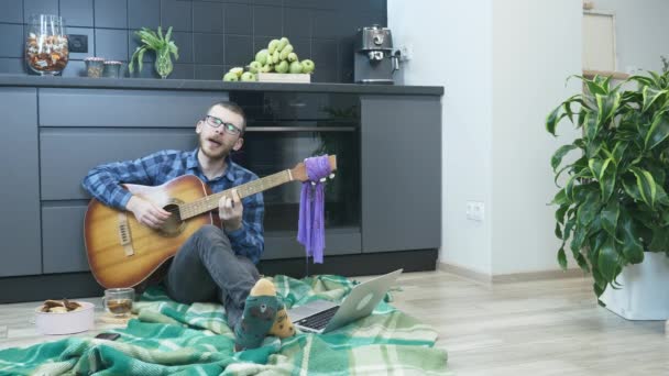 Férfi játszik akusztikus gitár és énekel romantikus dalszöveg ül a padlón, kényelmes lakás. Man gitározni otthon, pihentető alatt az önálló elszigetelés és a világjárvány karantén — Stock videók