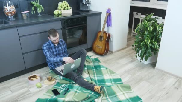 Mann öffnet Laptop-Computer und beginnt zu Hause zu arbeiten. Der männliche Student arbeitet während der Quarantäne zu Hause. Mann arbeitet auf Distanz an Notizbuch, während er in Küche auf dem Boden sitzt — Stockvideo