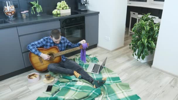 自宅のキッチンで床に座っているプロのギタリストチューニングギター。ギターは隔離中に家にいる。オンラインギターレッスン — ストック動画