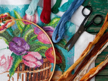 Lalelerin çapraz dikiş desenleri, mor, mavi, bej çiçekler eski ahşap bir arka planda. Masaüstü için ekran koruyucu. İğne işi, el yapımı, hobiler, boş zaman.