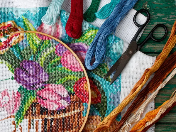 Lalelerin çapraz dikiş desenleri, mor, mavi, bej çiçekler eski ahşap bir arka planda. Masaüstü için ekran koruyucu. İğne işi, el yapımı, hobiler, boş zaman.