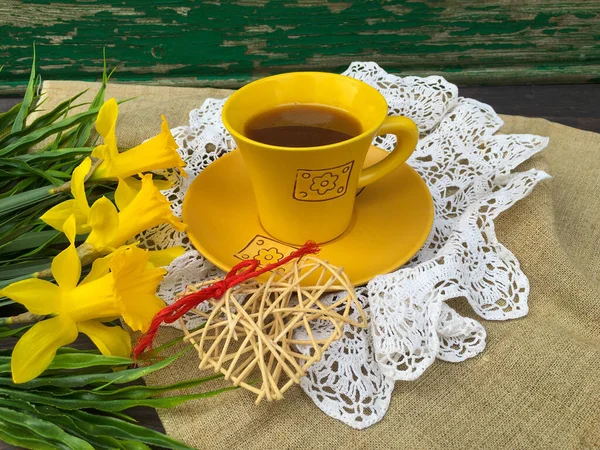 Cup of tea on a vintage table, yellow daffodils, white crocheted napkin.
