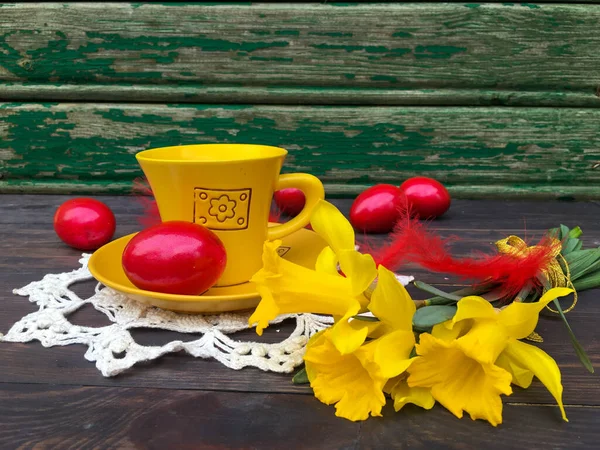 Easter red eggs, a cup of tea on a vintage table, yellow daffodils, white crocheted napkin. Background, wallpaper or postcard.
