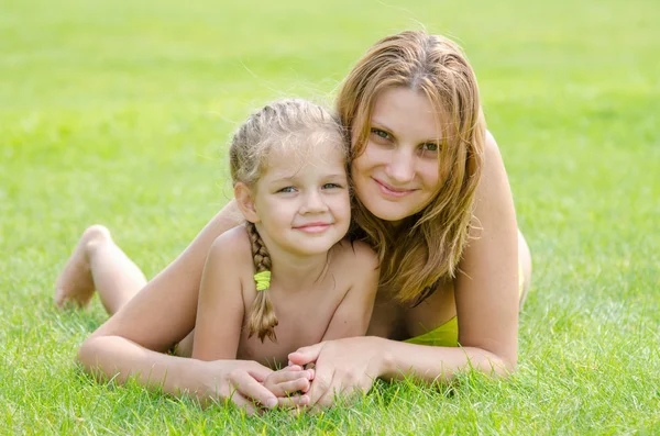 Jeune mère et fille de cinq ans étreignant couché sur l'herbe verte et regardant vers le cadre — Photo