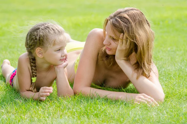 Молодая мать и пятилетняя дочь лежат на зеленой траве и смотрят друг на друга. — стоковое фото