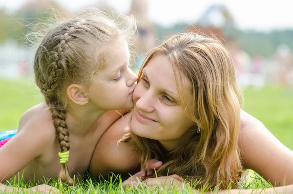 Die fünfjährige Tochter küsst ihre Mutter, die auf dem grünen Rasen liegt — Stockfoto