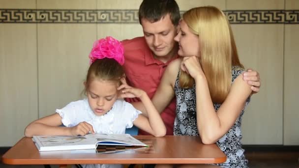 Pappa och mamma tittar kärleksfullt på min dotter första-väghyvel som gör sina läxor — Stockvideo