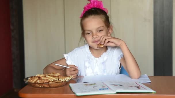 Niña de siete años colegiala haciendo deberes bocadillos galletas — Vídeo de stock