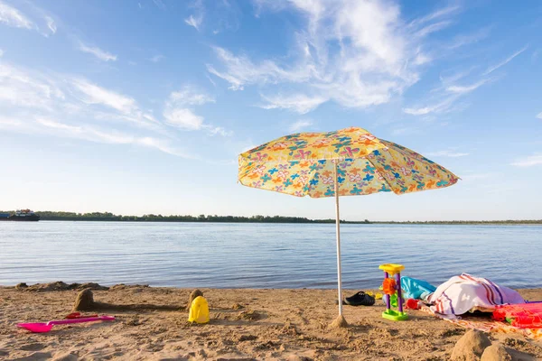 Sonnenschirm am Flussufer, unter dem die verstreuten Gegenstände und Spielzeuge — Stockfoto