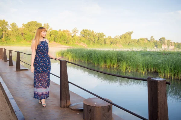 La encantadora jovencita caminando por el puente sobre el río al amanecer — Foto de Stock