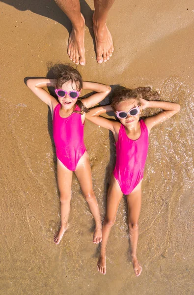 Två flickor Ligg på ryggen på surf av sea sandstranden beach, finns ett antal vuxna mänsklig fot — Stockfoto