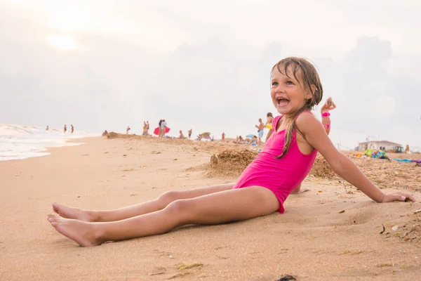 Пятилетняя девочка сидит на пляже на вечернем берегу моря в пасмурный день — стоковое фото
