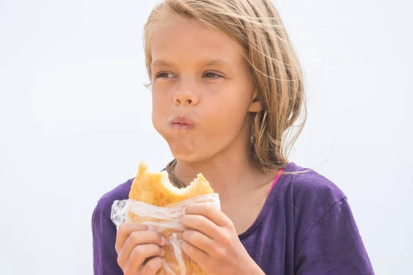 食欲と空腹の少女がビーチでおいしいケーキをかみ砕く — ストック写真
