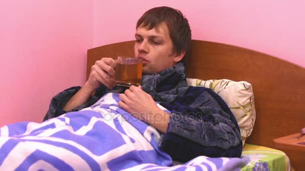 A sick man lying in bed and drink hot tea — Stock Video