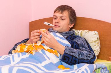 A sick kid with a thermometer in her mouth lying in bed and eating tangerines clipart