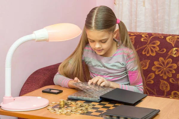 Chica en la mesa hojeando el álbum con monedas —  Fotos de Stock