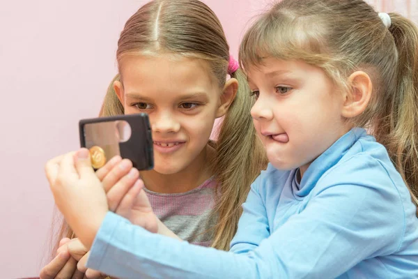 Dos niños consideraban una moneda a través de una lupa —  Fotos de Stock