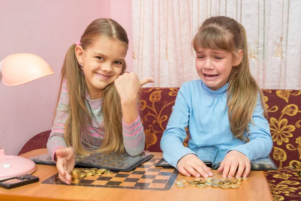 Two girls at the table collected montki one cries, the other laughs at it — Stock Photo, Image