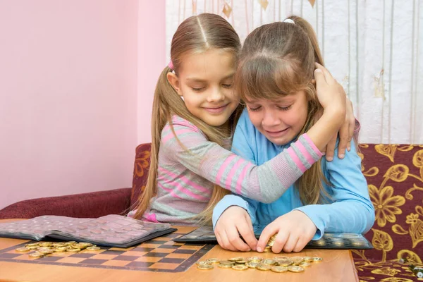 De oudere zus troostend huilende jongere zus, die een stapel van munten verzamelt — Stockfoto