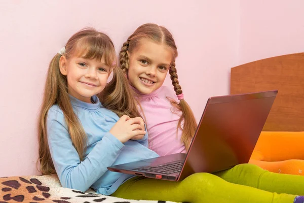 Två tjejer sitter på en säng med en laptop och en rolig ser i ramen — Stockfoto