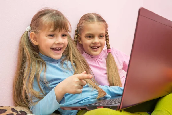 Две девушки весело смотрят на ноутбук и смеются, одна указывает на экран — стоковое фото