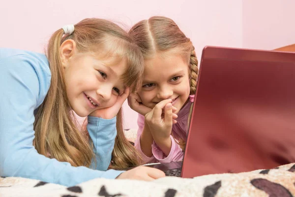 Сестры смотрят мультик на ноутбуке и смеются над смешным моментом — стоковое фото
