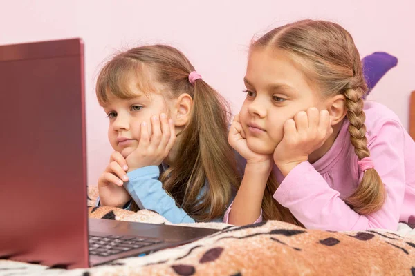 Två flickor på magen på sängen tittar på laptop skärmen — Stockfoto