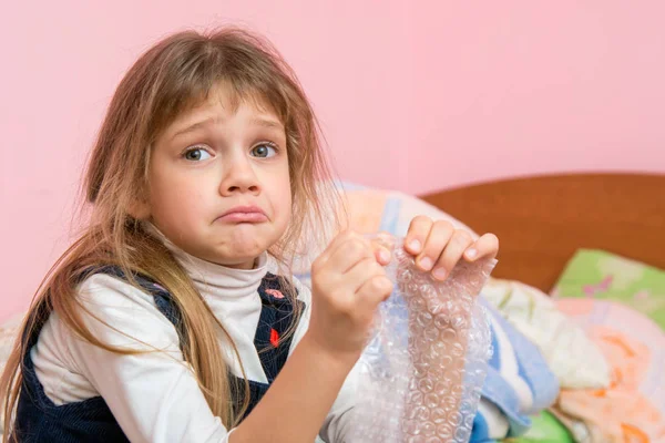 Upset girl pouting cheeks eats bubbles packaging film and looked for someone — Stock Photo, Image