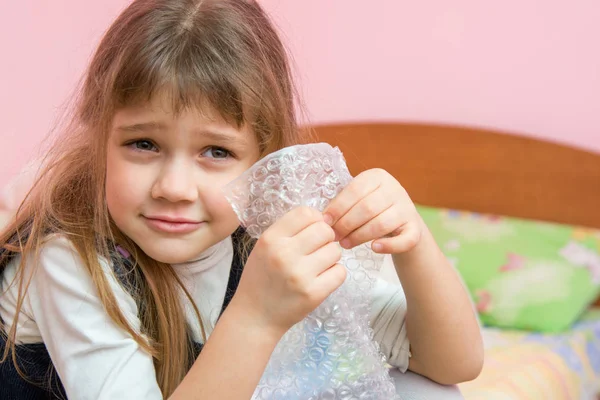 Fünfjähriges Mädchen hört zu, wie Blasen auf der Verpackung platzen — Stockfoto