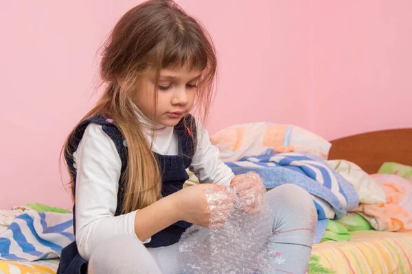 Triste fille assise sur le lit et mange des bulles sur le film d'emballage — Photo