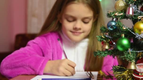 Девушка пишет письмо Санта-Клаусу, акцент делается на меховое дерево перед ней — стоковое видео
