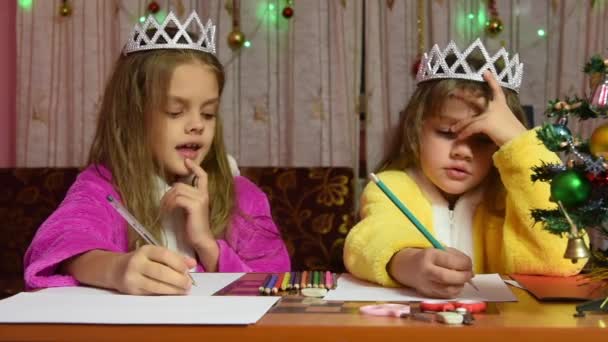 Две девушки в халатах, сидящие за столом и пишущие письмо Санта Клаусу, одна из них думает смешно — стоковое видео