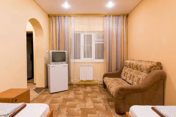 El interior de una pequeña habitación con sofá cama y dos camas individuales, ventana, TV y nevera — Foto de Stock