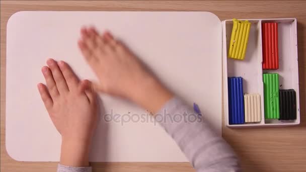 L'enfant roule une boule de plasticine main sur la carte pour la modélisation, gros plan, vue du dessus — Video
