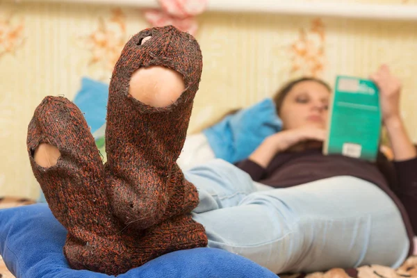 这个女孩正躺在沙发上，正在读一本书，在前景的多孔的袜子 — 图库照片