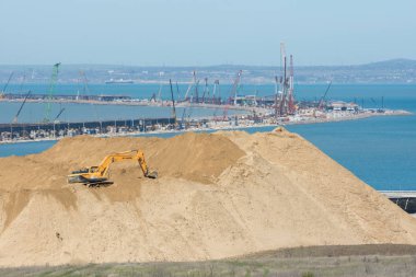 Taman, Rusya - 15 Nisan 2017: Ön planda büyük bir toprak yığını ve 2017 Nisan ayı itibarıyla Boğaz boyunca inşa halindeki köprünün kıvrımı