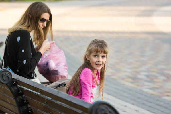 Шестилетняя девочка и мама сидели на скамейке для прогулки, девушка радостно посмотрела на рамку — стоковое фото