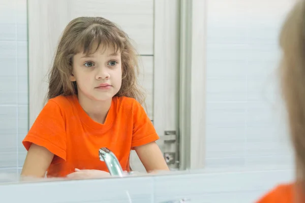 Ragazza di sette anni si guarda allo specchio, in bagno — Foto Stock