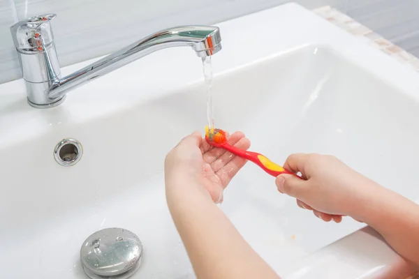 Ребенок промывает зубную щетку под проточной водой — стоковое фото