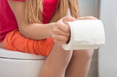 Bir kız ellerini Tuvalette otururken, bir rulo tuvalet kağıdı tutuyor