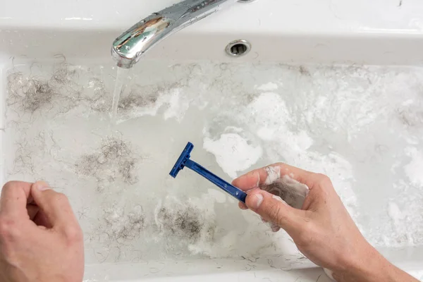 El hombre se afeita, la vista de las manos con una afeitadora y el lavabo con agua sucia — Foto de Stock